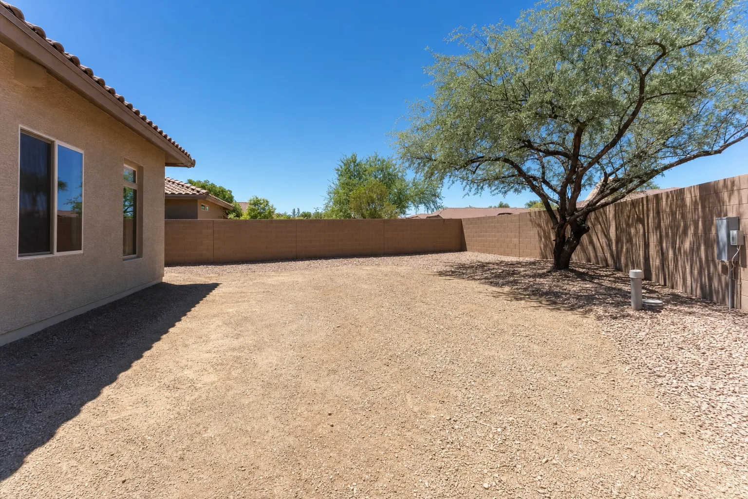 Empty gravel backyard lot in Mesa, Arizona with a block wall, mesquite tree and utility stubs, the kind of parcel a Site Discovery visit measures
