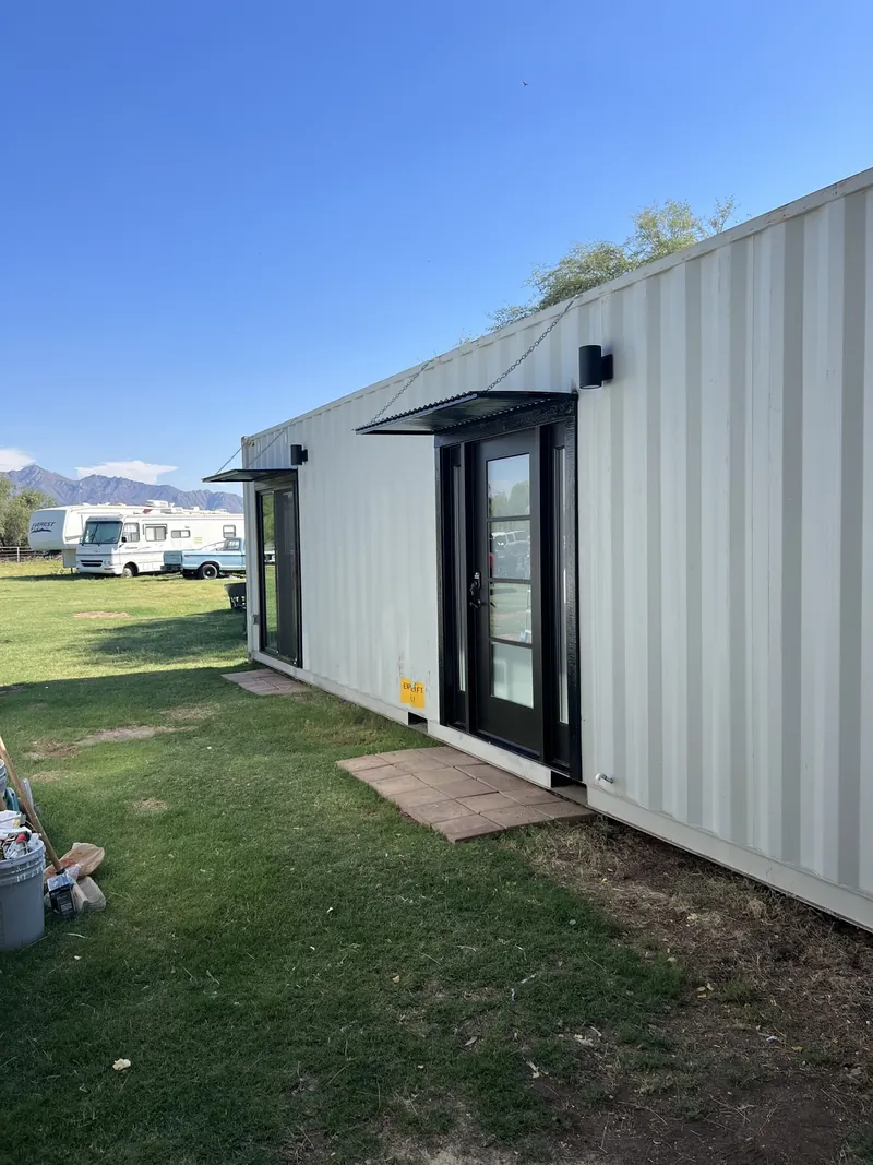 Finished 40 foot silver container home set on a level green lot with a covered entry awning